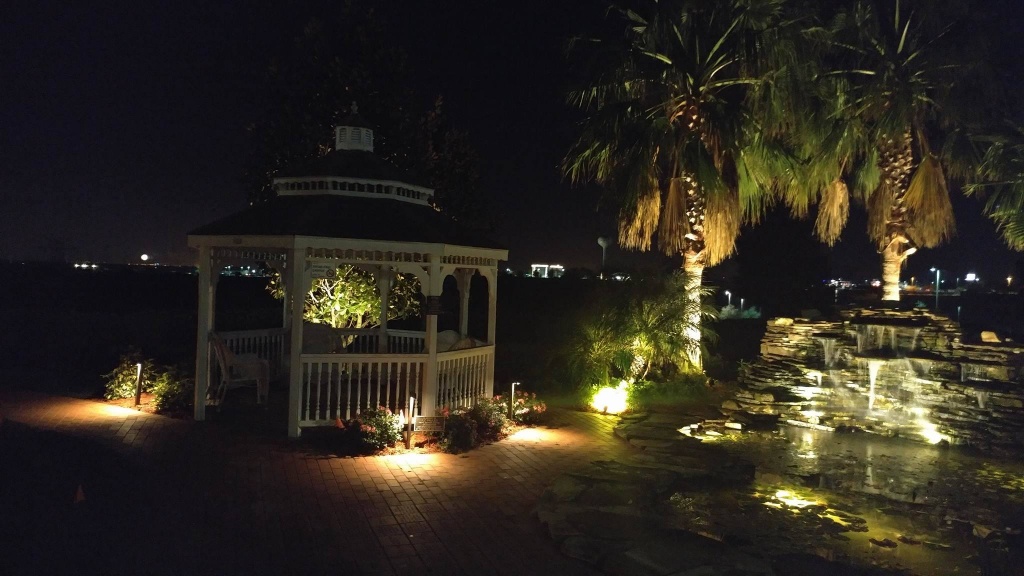 Outdoor gazebo and water feature lit up at night with landscape lighting